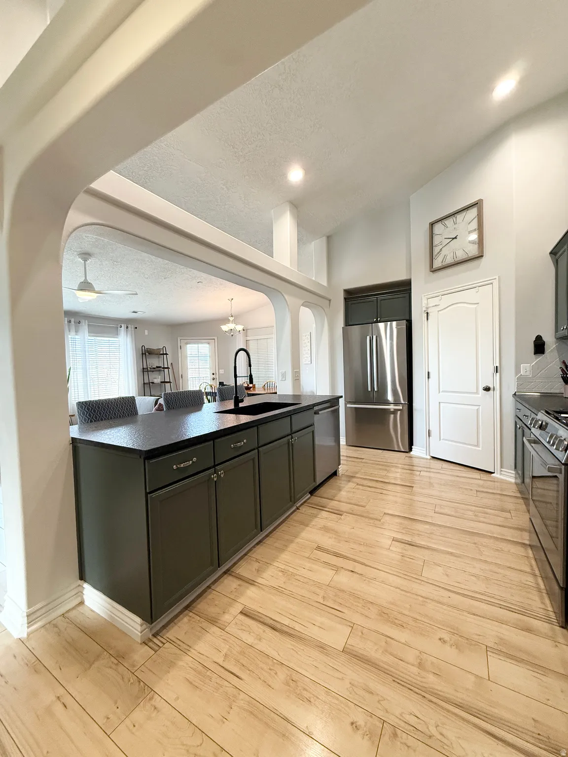 Kitchen featuring arched walkways, dark countertops, stainless steel appliances, light wood finished floors, and a kitchen bar