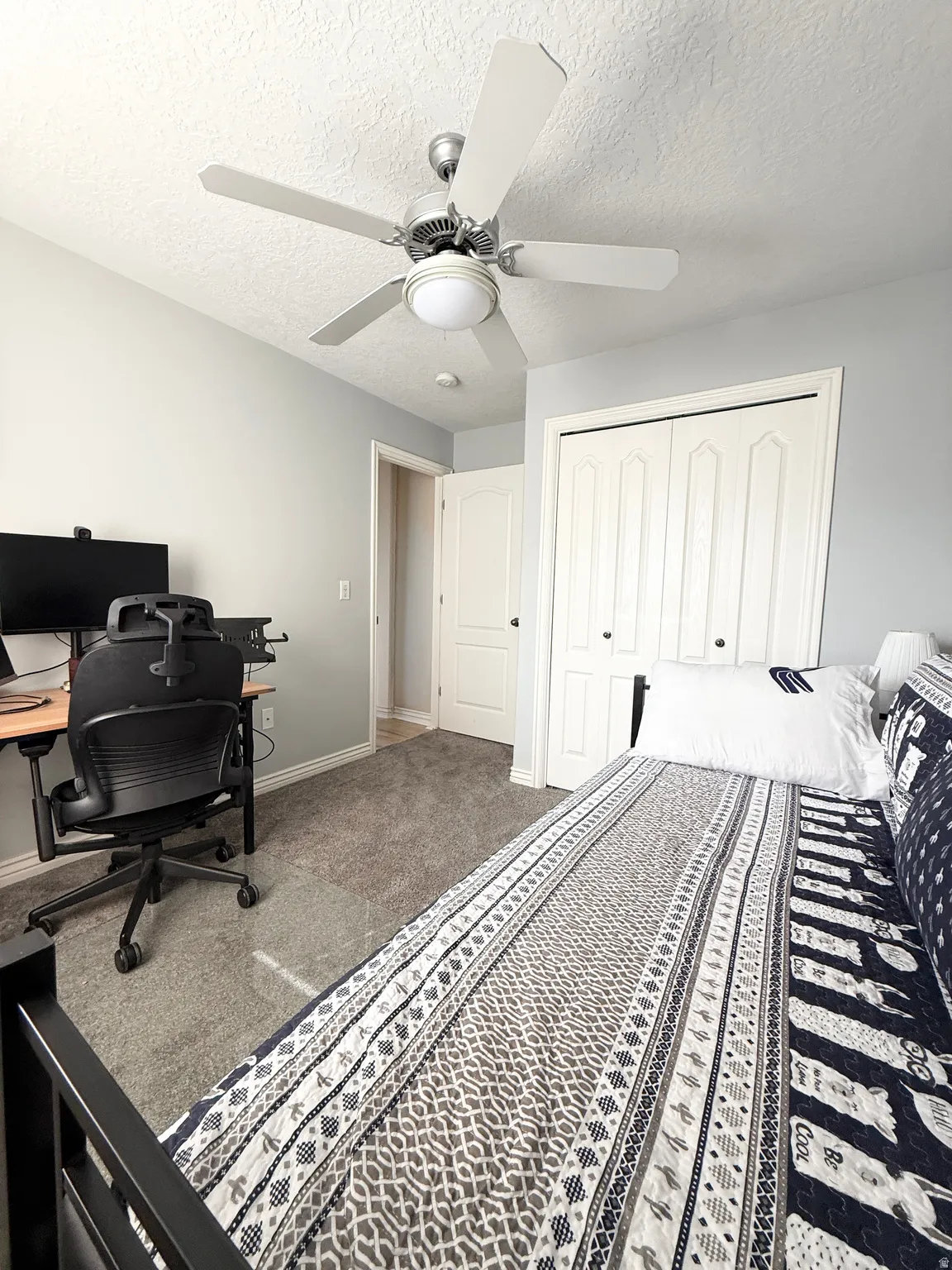 Carpeted bedroom featuring a desk, ceiling fan, a closet, and a textured ceiling