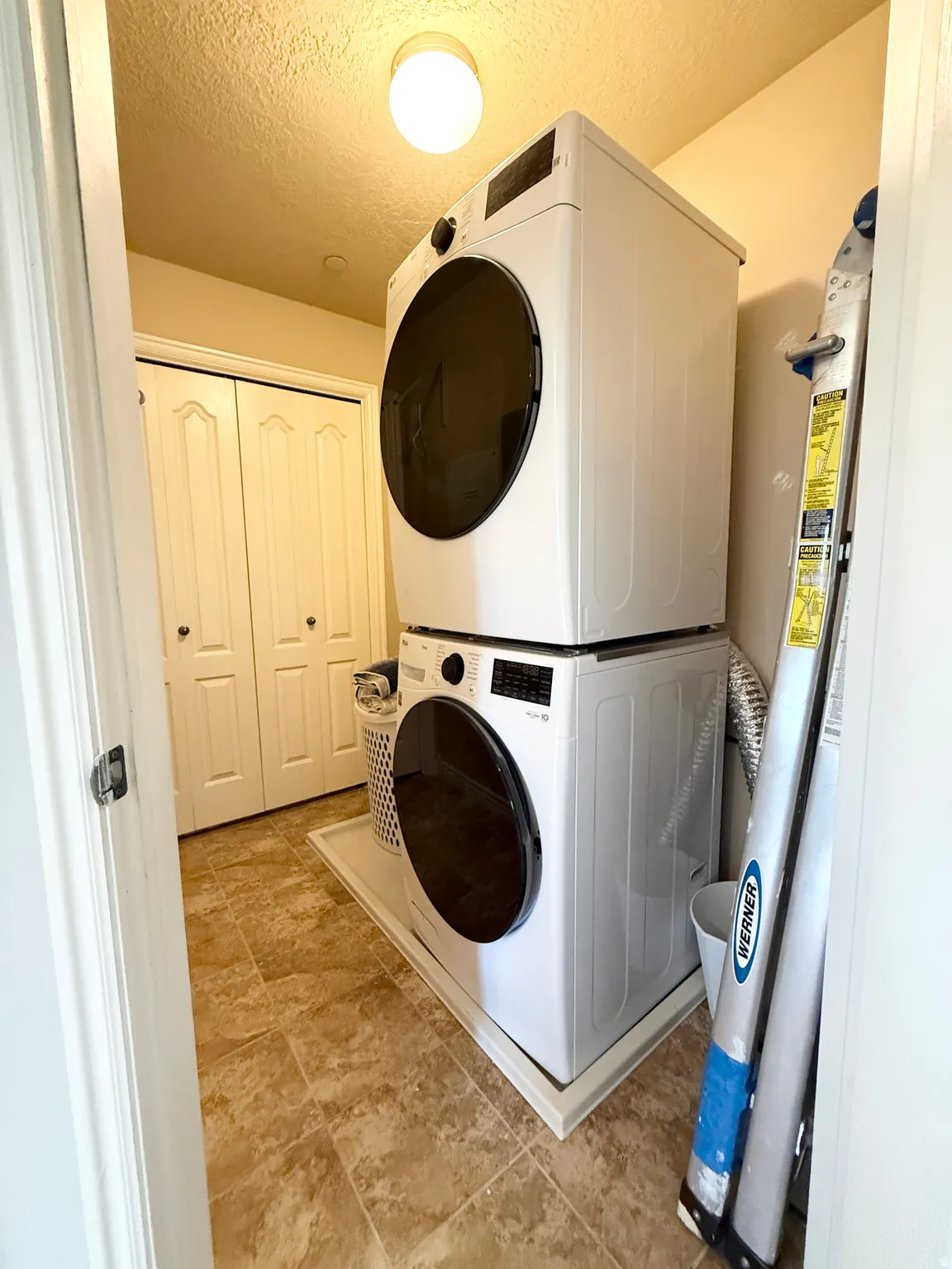 Laundry room featuring a textured ceiling, stacked washing machine and dryer, and water heater
