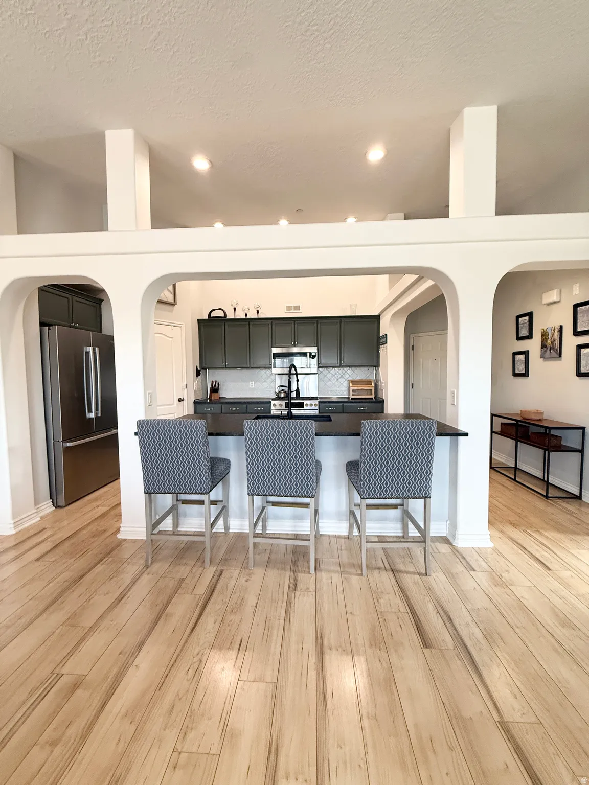 Kitchen with arched walkways, a kitchen breakfast bar, dark countertops, stainless steel appliances, and a textured ceiling