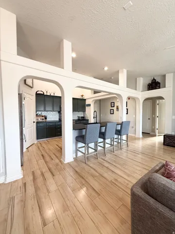 Kitchen with arched walkways, a breakfast bar area, open floor plan, dark countertops, and light wood-style flooring