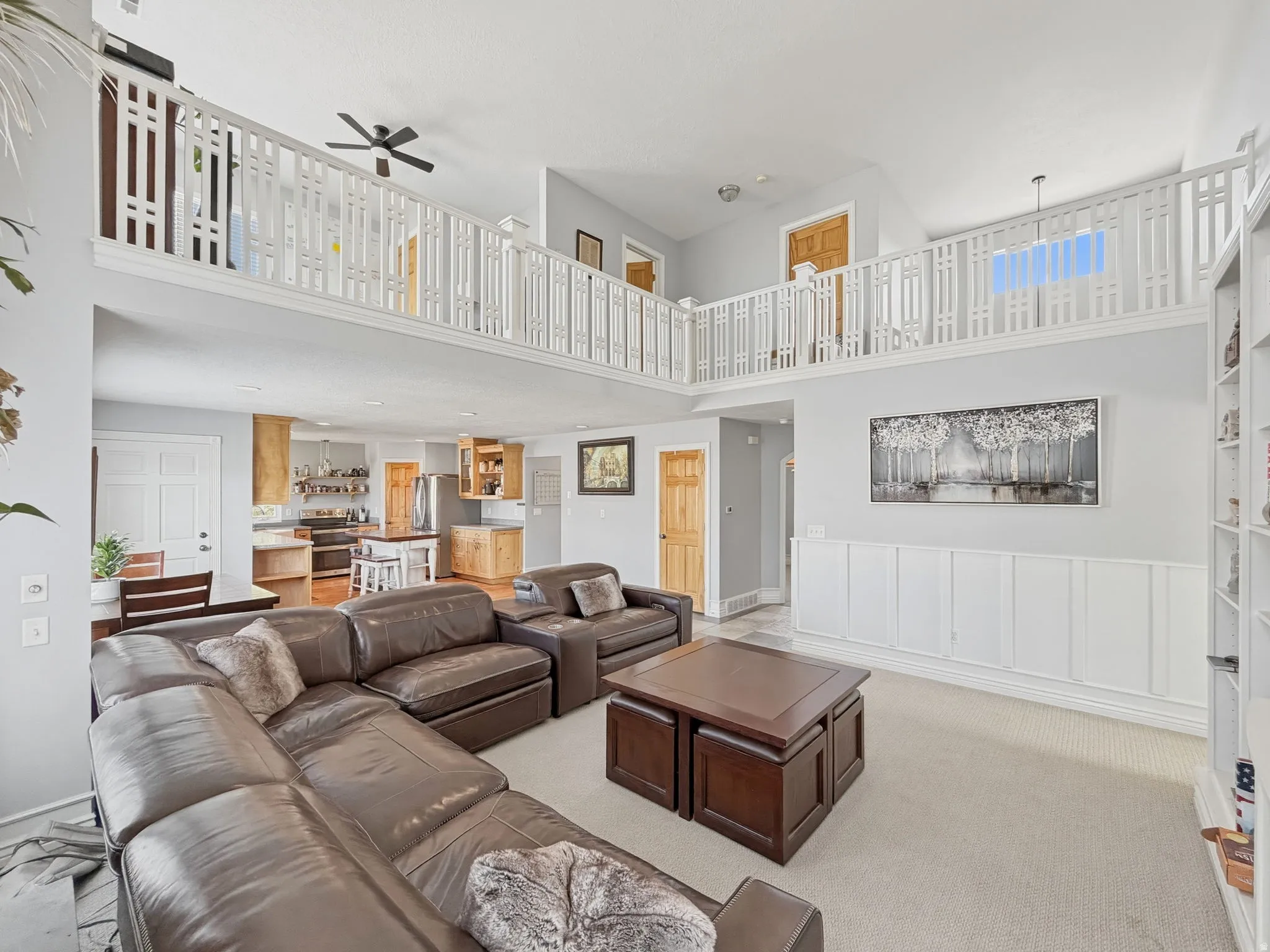 Living room with a ceiling fan, light colored carpet, a decorative wall, and a high ceiling