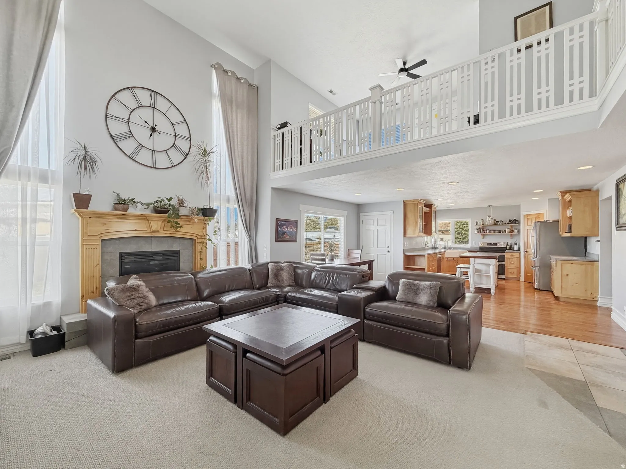 Living room with a ceiling fan, a tile fireplace, light colored carpet, a high ceiling, and recessed lighting