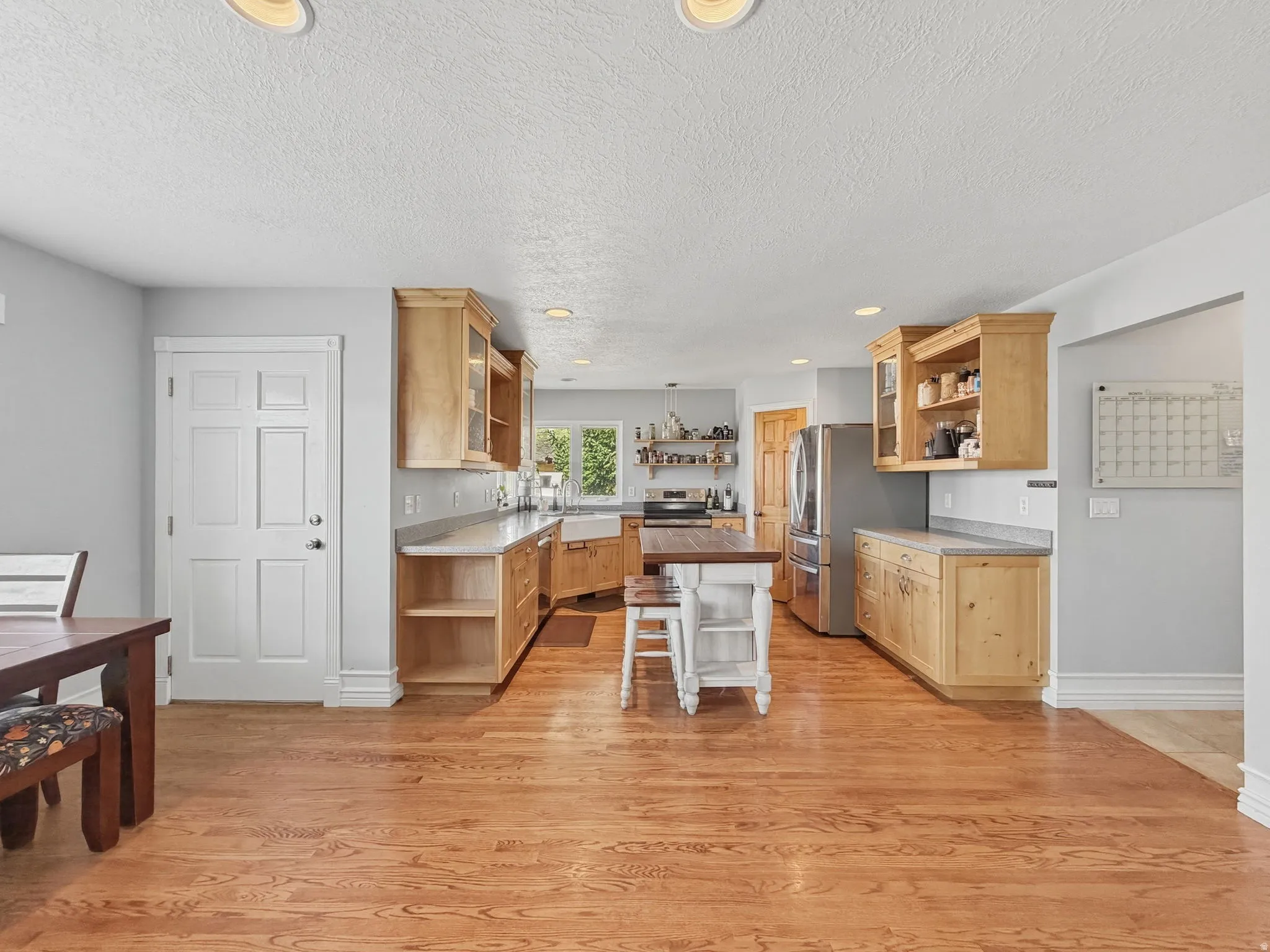 Kitchen featuring open shelves, glass insert cabinets, stainless steel appliances, light wood-style flooring, and a textured ceiling