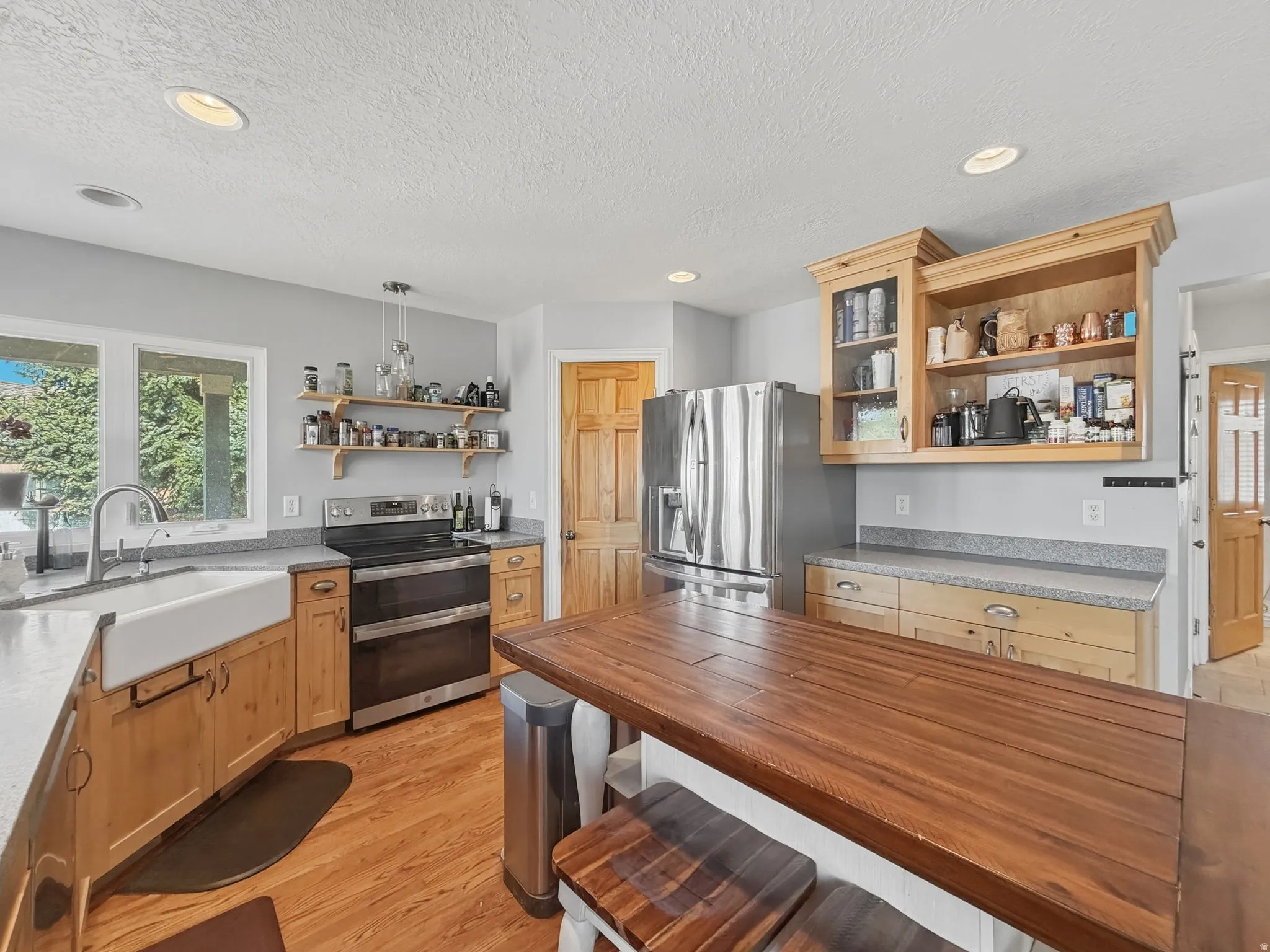 Kitchen with open shelves, plenty of natural light, stainless steel appliances, light wood-style flooring, and a textured ceiling