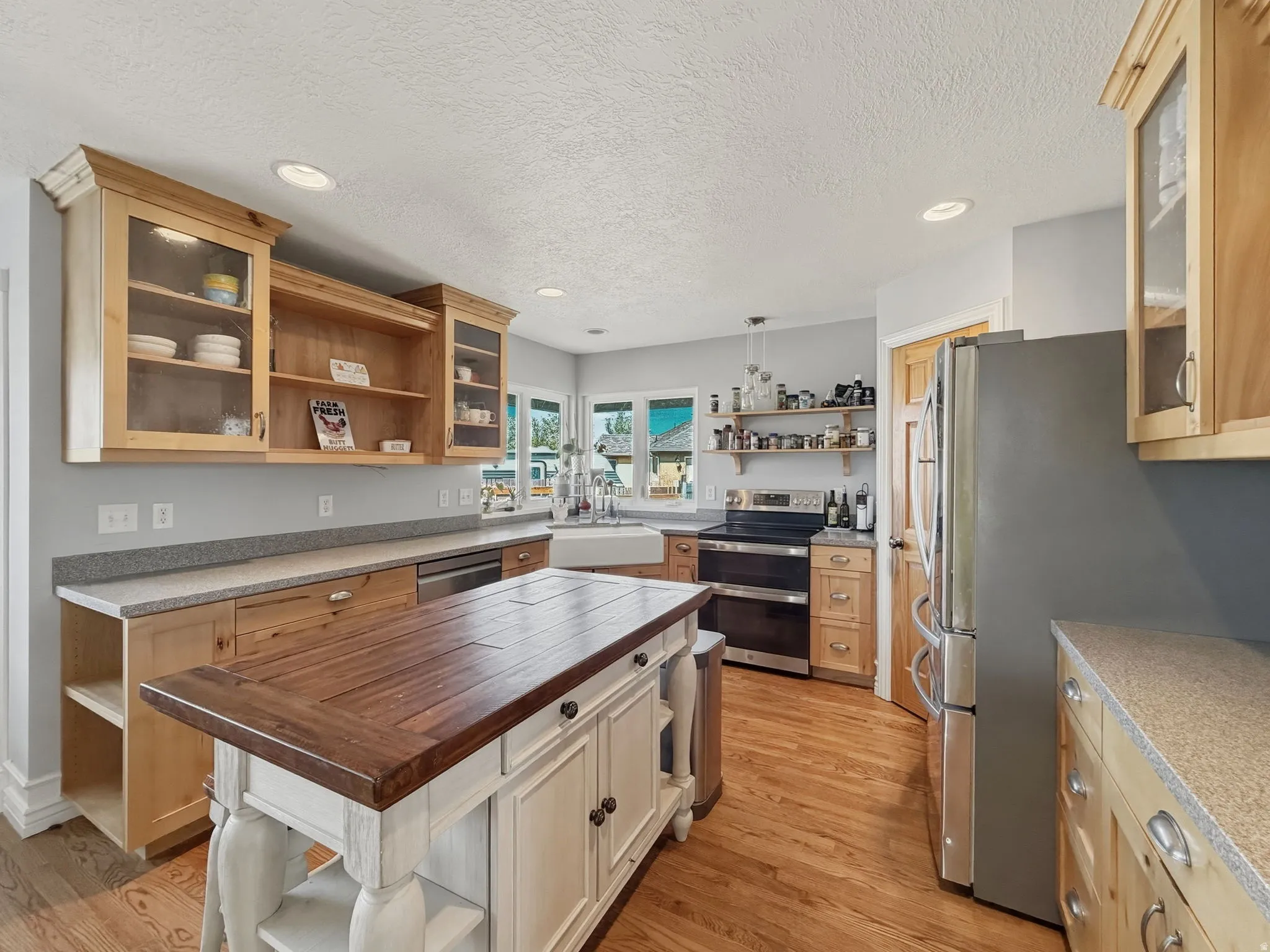 Kitchen with open shelves, glass insert cabinets, butcher block counters, recessed lighting, and a textured ceiling