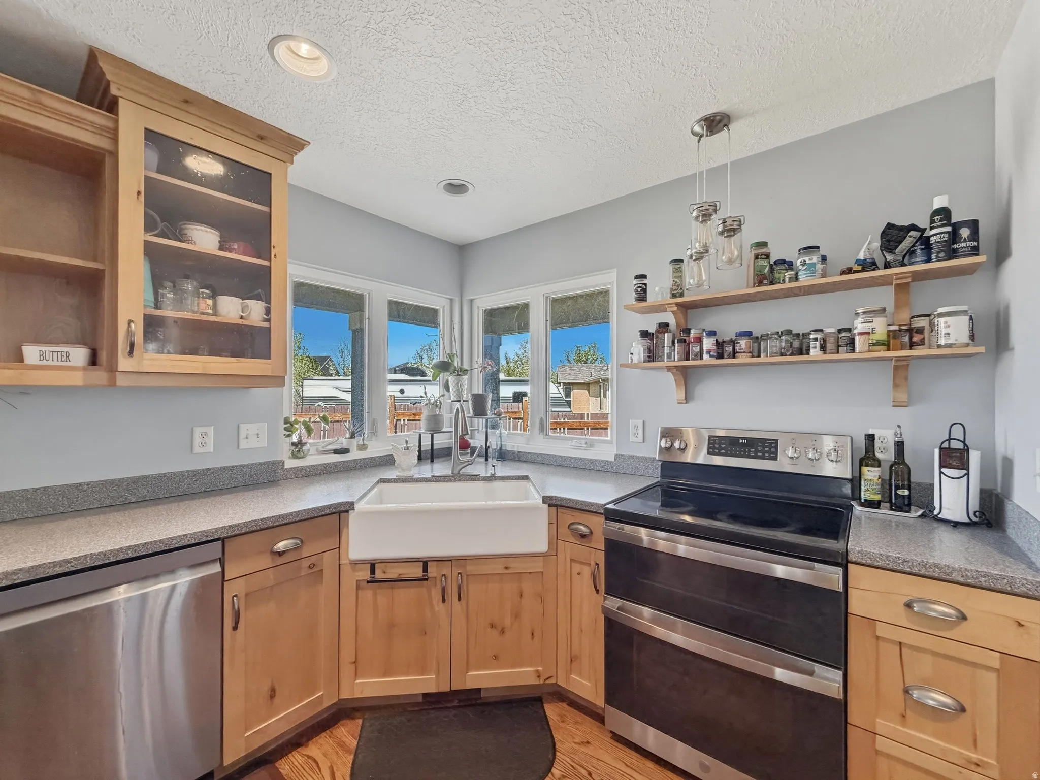 Kitchen featuring stainless steel appliances, open shelves, glass fronted cabinets, decorative light fixtures, and a textured ceiling