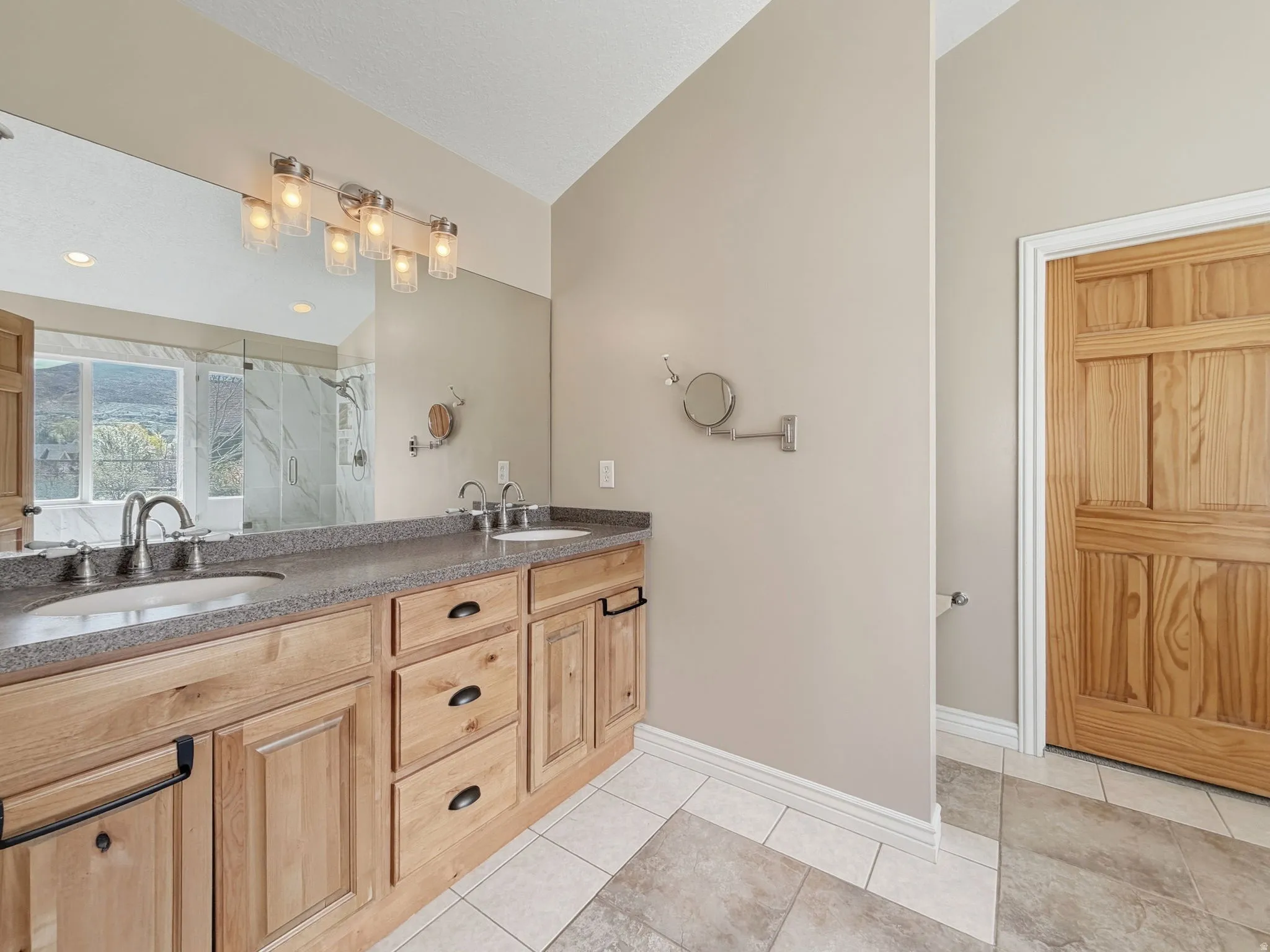 Full bathroom with a marble finish shower, double vanity, and light tile patterned floors