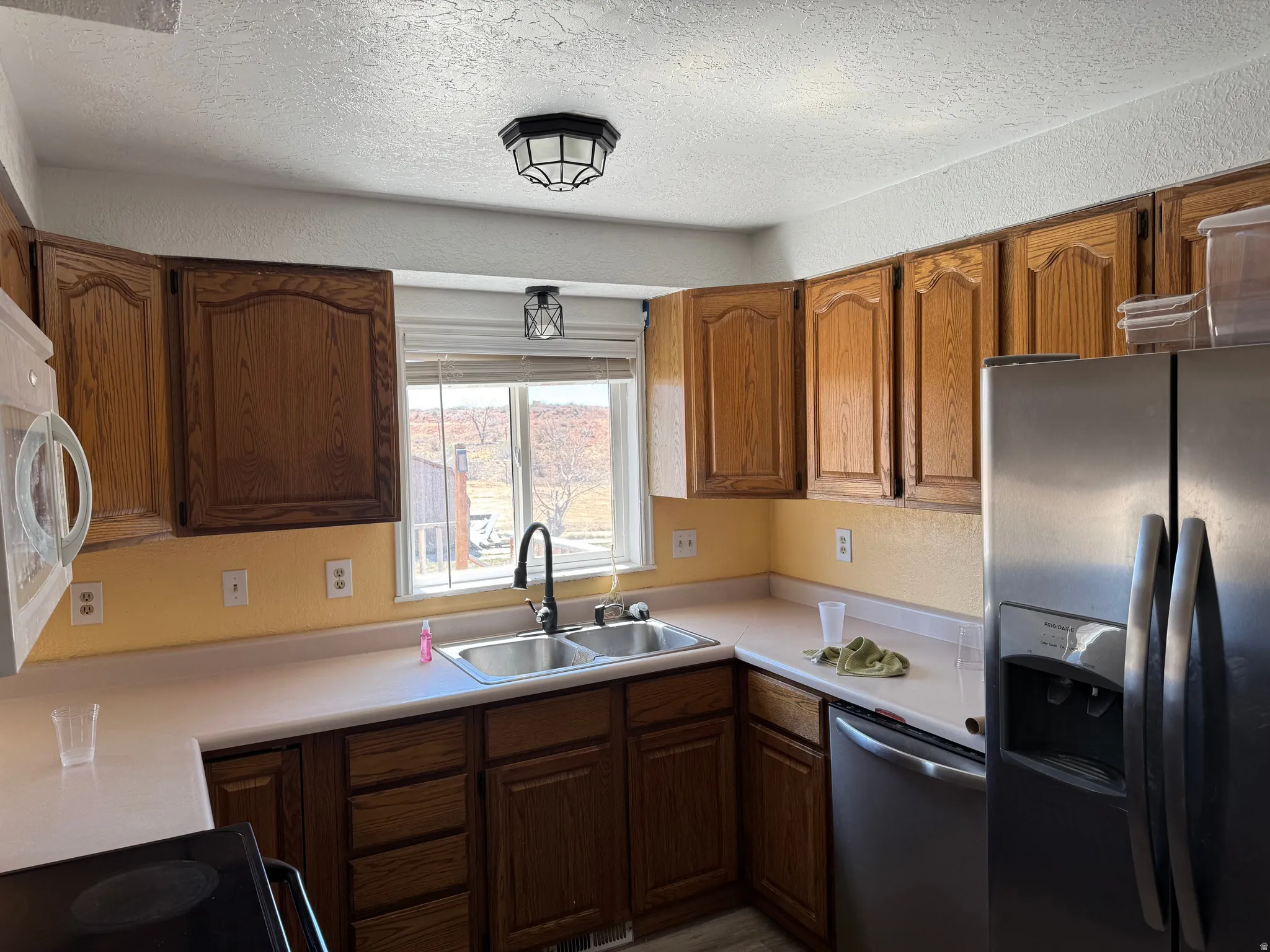 Kitchen with stainless steel appliances, light countertops, wood finish cabinets, a textured ceiling, and a textured wall