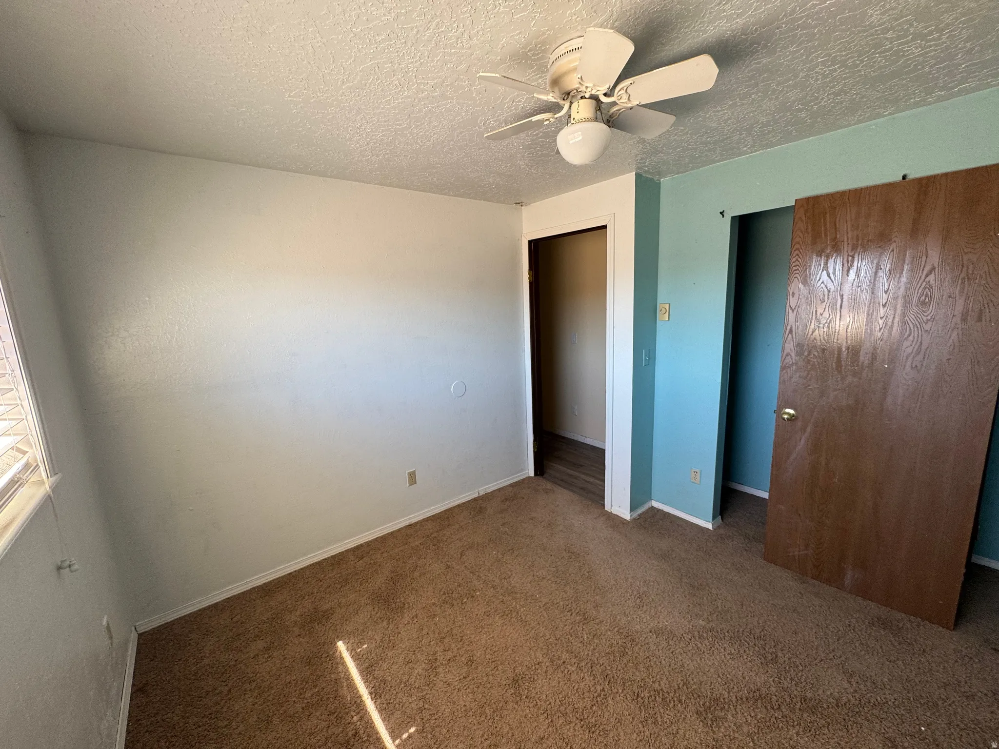 Unfurnished bedroom with dark carpet, ceiling fan, and a textured ceiling