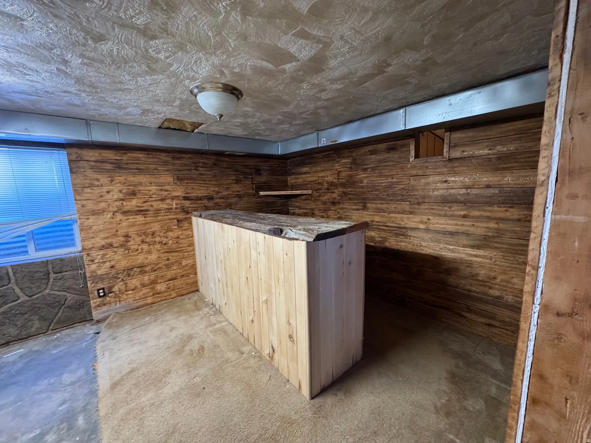 Bar with wooden walls, dark carpet, and light wood finish cabinetry