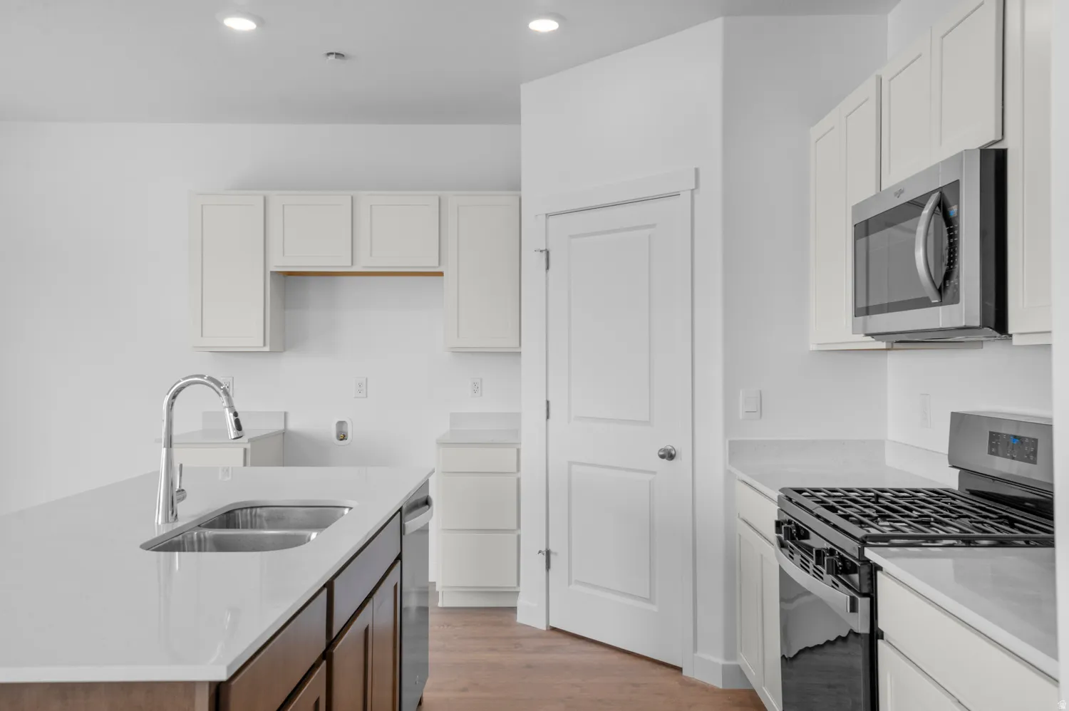 Two tone kitchen with stainless steel appliances, a kitchen island with sink, light stone countertops, dual tone cabinetry, and light wood-type flooring