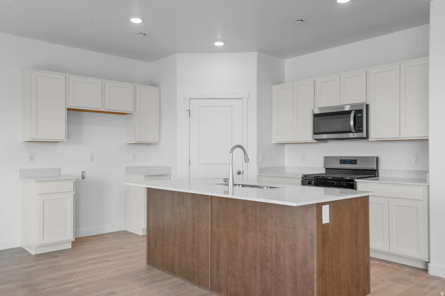 Dual tone kitchen featuring a kitchen island with sink, stainless steel microwave, range with gas cooktop, light wood-style flooring, and light stone counters