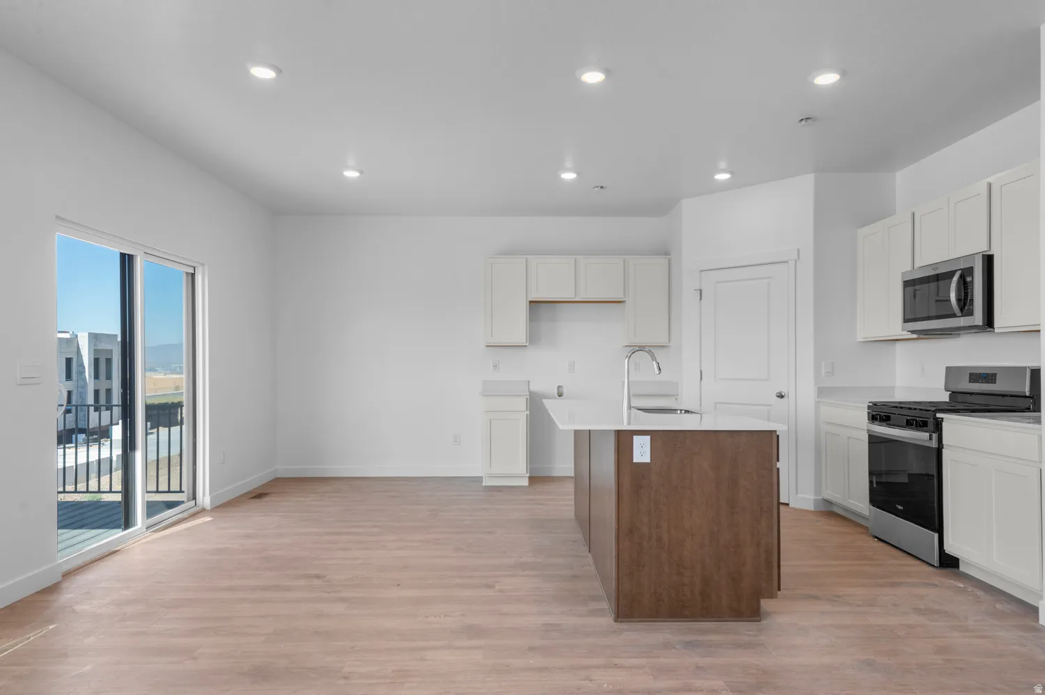 Dual tone kitchen with stainless steel appliances, recessed lighting, a center island with sink, light wood finished floors, and light stone countertops