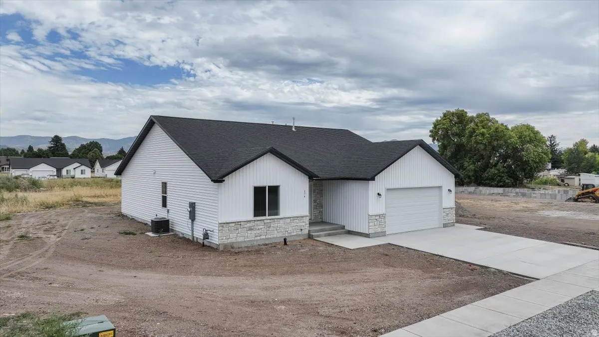 Modern farmhouse featuring concrete driveway, stone siding, a garage, and a shingled roof