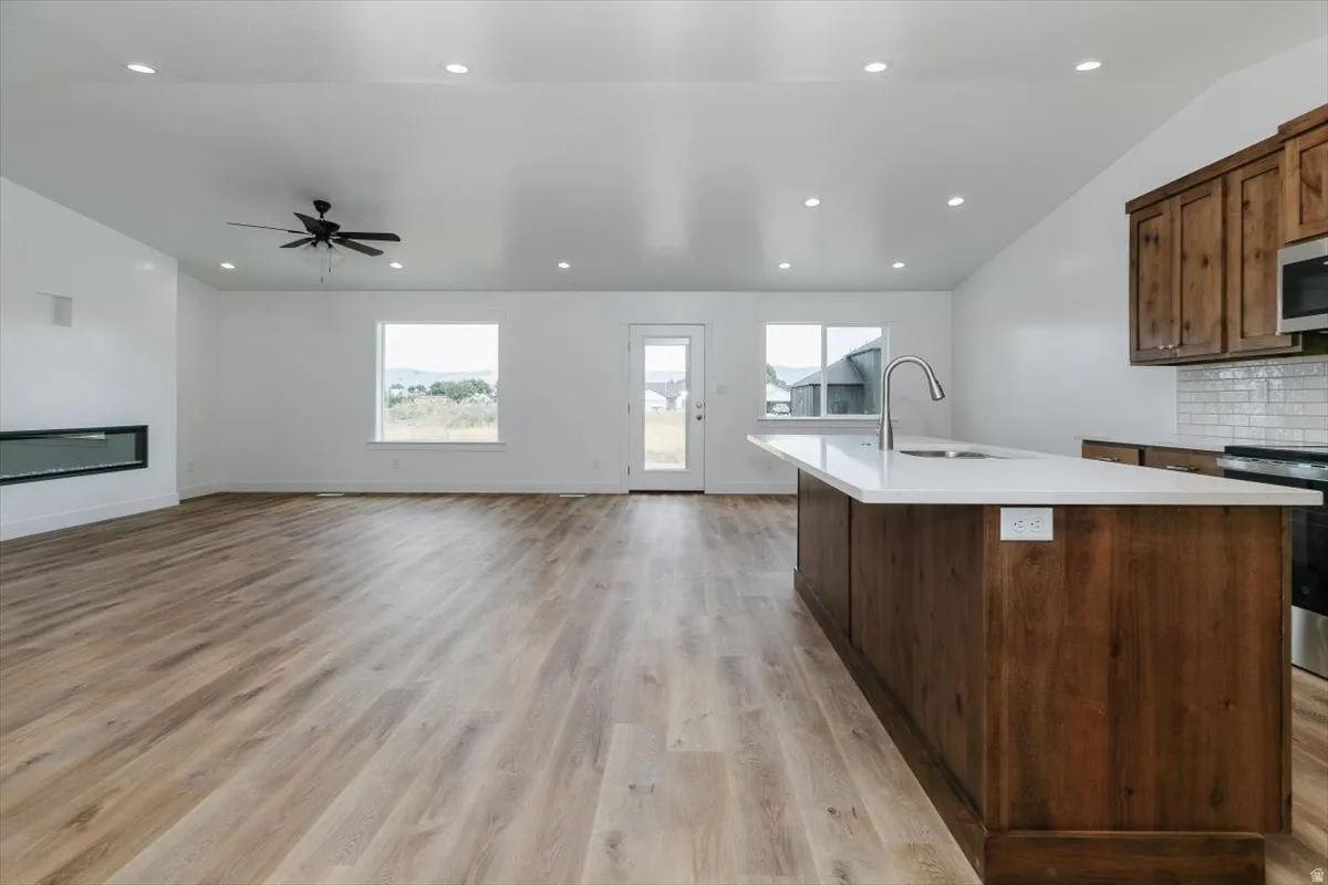 Kitchen with an island with sink, light wood-style floors, a glass covered fireplace, open floor plan, and decorative backsplash