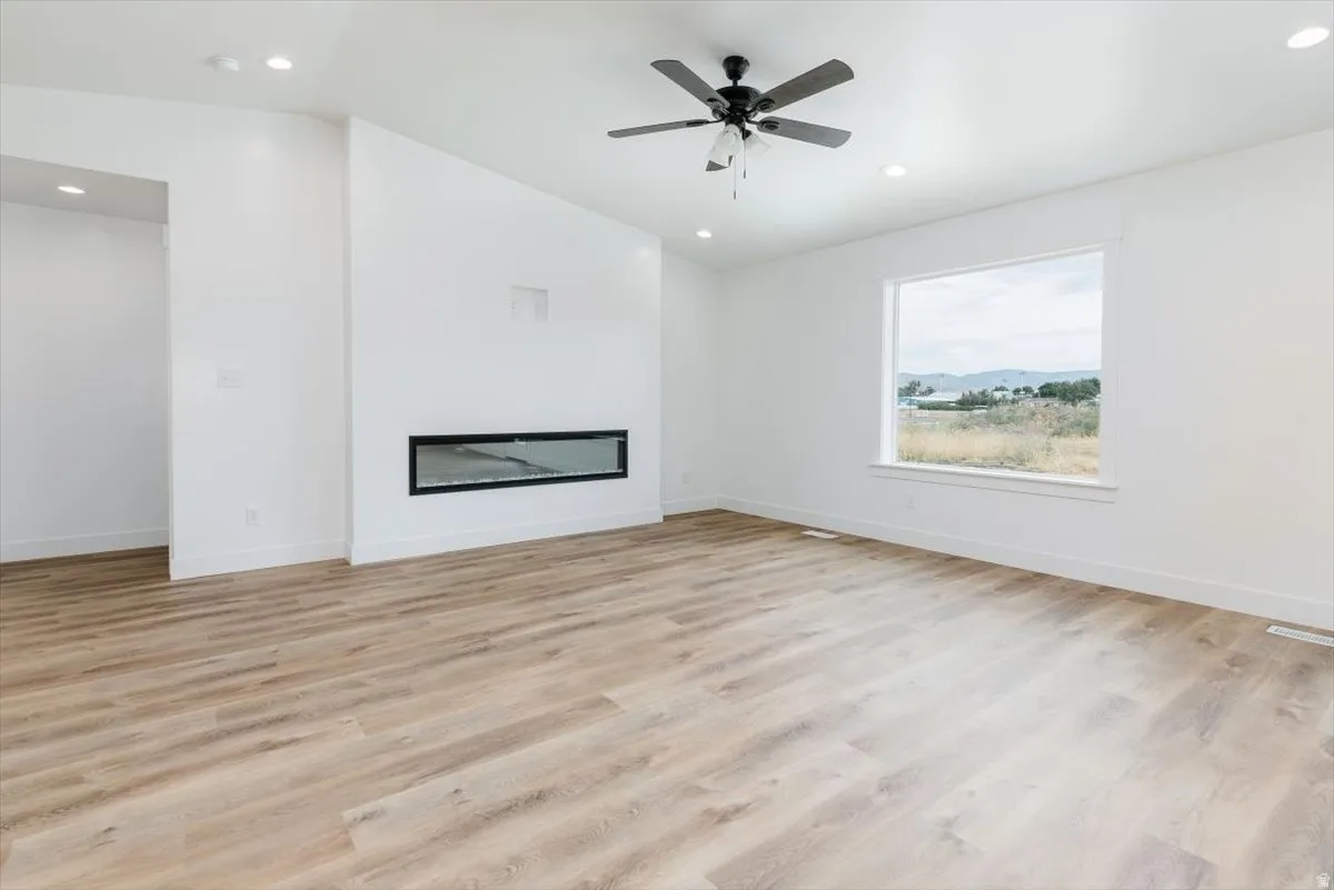 Unfurnished living room featuring light wood-type flooring, vaulted ceiling, a glass covered fireplace, recessed lighting, and a ceiling fan