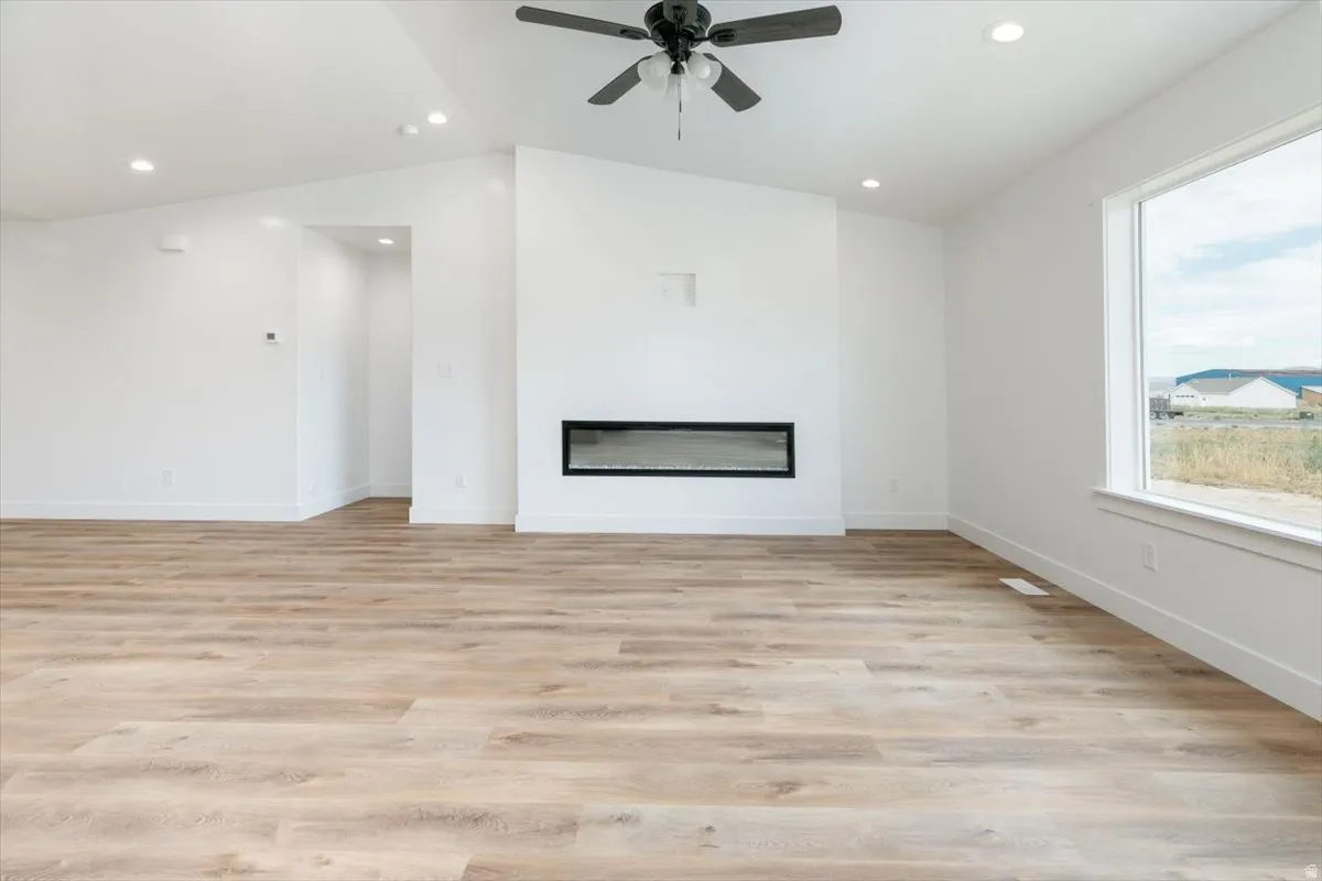 Unfurnished living room featuring ceiling fan, light wood-style flooring, a glass covered fireplace, recessed lighting, and lofted ceiling