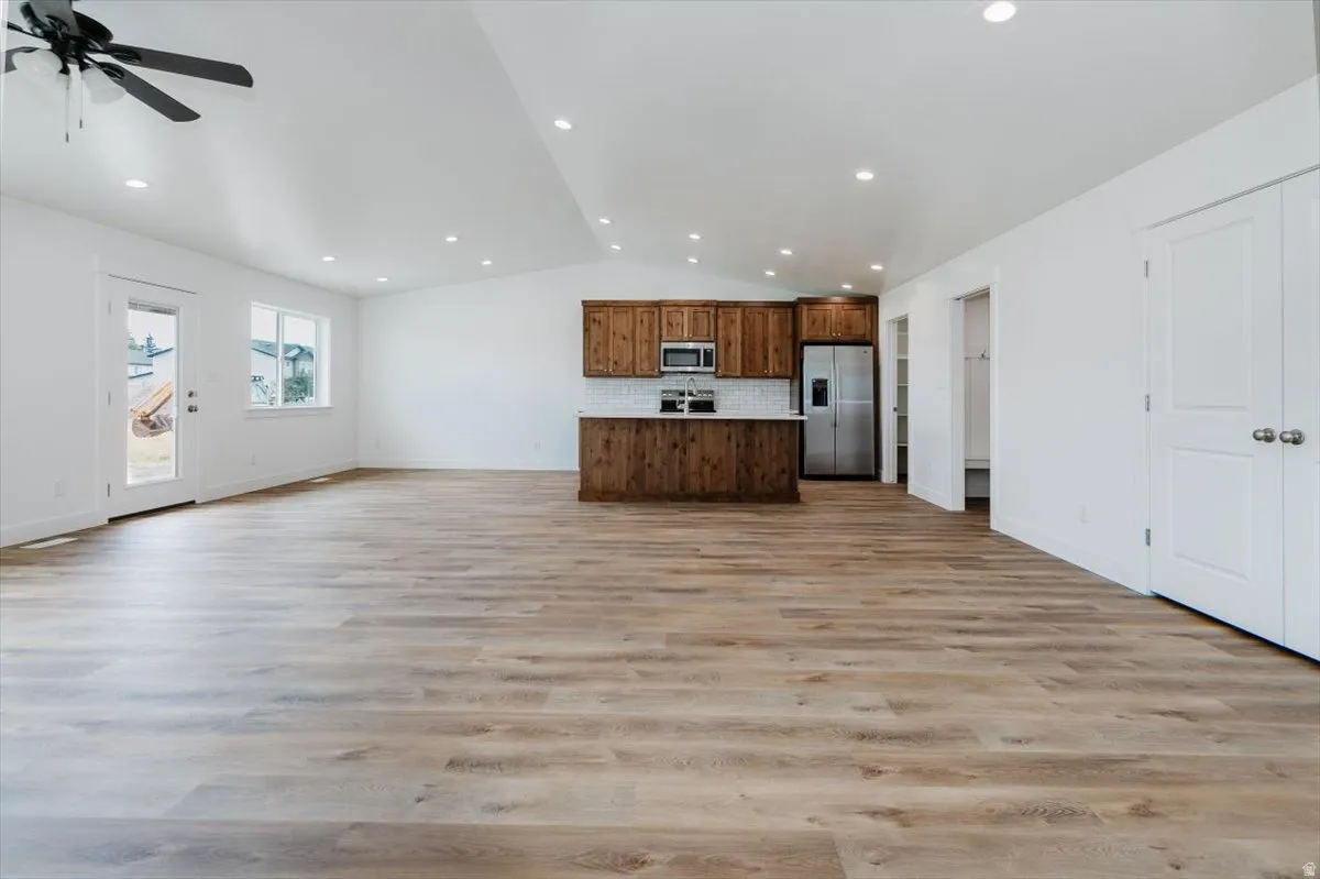 Kitchen featuring open floor plan, lofted ceiling, stainless steel appliances, light countertops, and tasteful backsplash