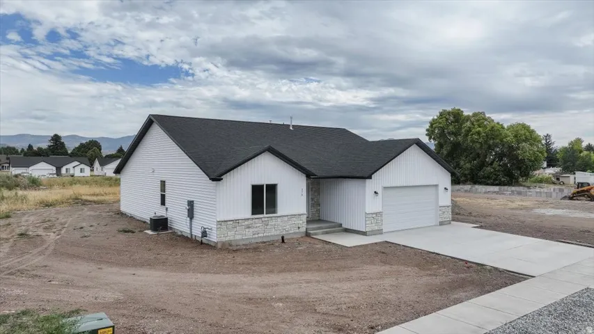 Modern farmhouse featuring concrete driveway, stone siding, a garage, and a shingled roof