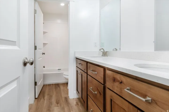 Full bathroom with double vanity, light wood-type flooring, and washtub / shower combination