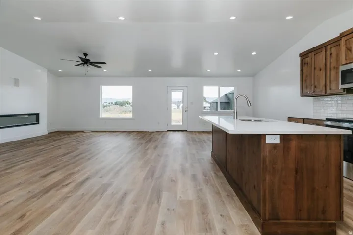 Kitchen with an island with sink, light wood-style floors, a glass covered fireplace, open floor plan, and decorative backsplash