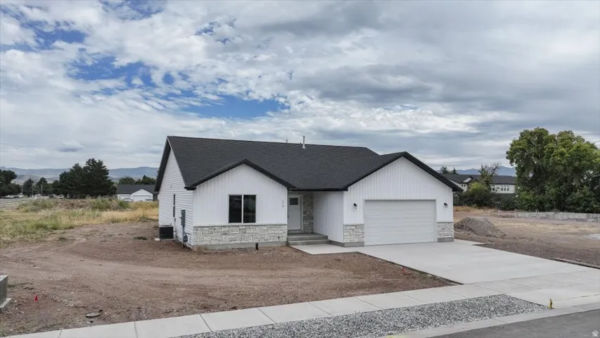 View of front of home with concrete driveway, stone siding, a garage, and roof with shingles