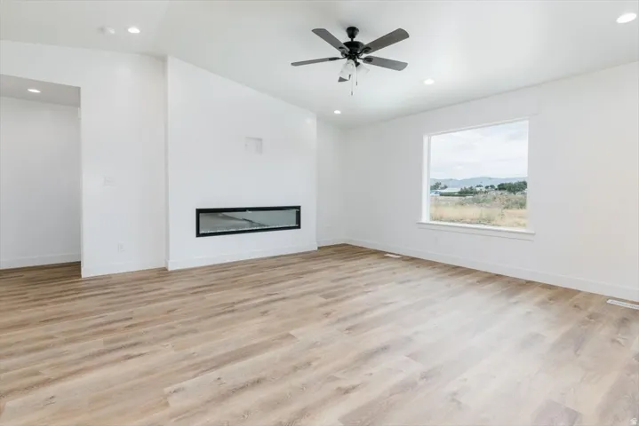 Unfurnished living room featuring light wood-type flooring, vaulted ceiling, a glass covered fireplace, recessed lighting, and a ceiling fan