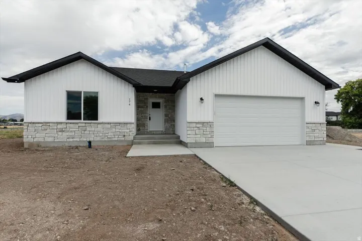 View of front of home featuring stone siding, an attached garage, driveway, and board and batten siding