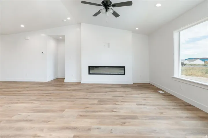 Unfurnished living room featuring ceiling fan, light wood-style flooring, a glass covered fireplace, recessed lighting, and lofted ceiling