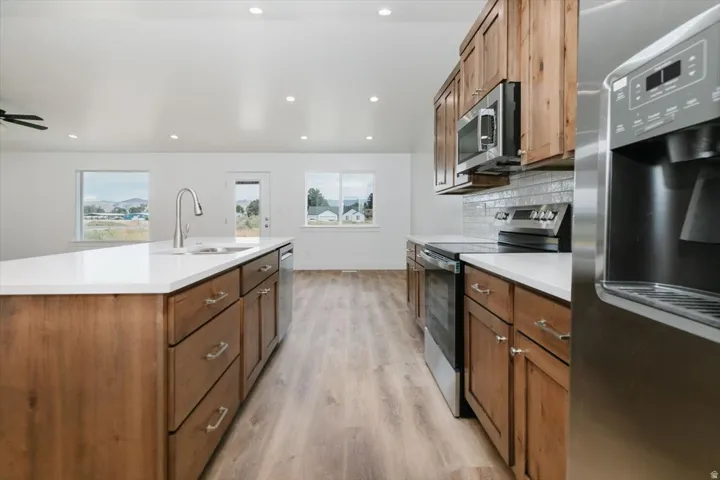 Kitchen with stainless steel appliances, wood finish cabinetry, light wood-style floors, tasteful backsplash, and recessed lighting