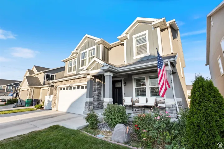 Craftsman-style house with an attached garage, covered porch, driveway, stone siding, and board and batten siding