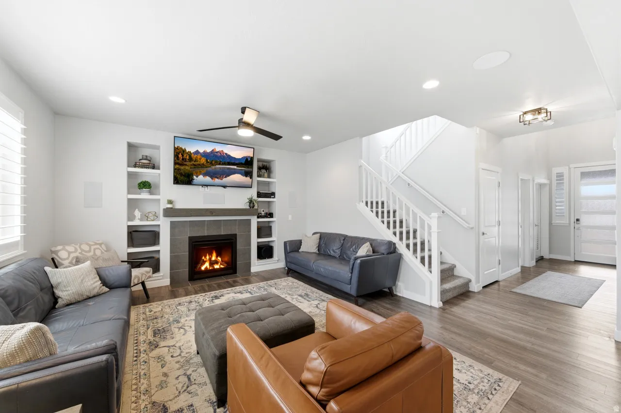 Living area with wood finished floors, a ceiling fan, a tile fireplace, built in features, and recessed lighting