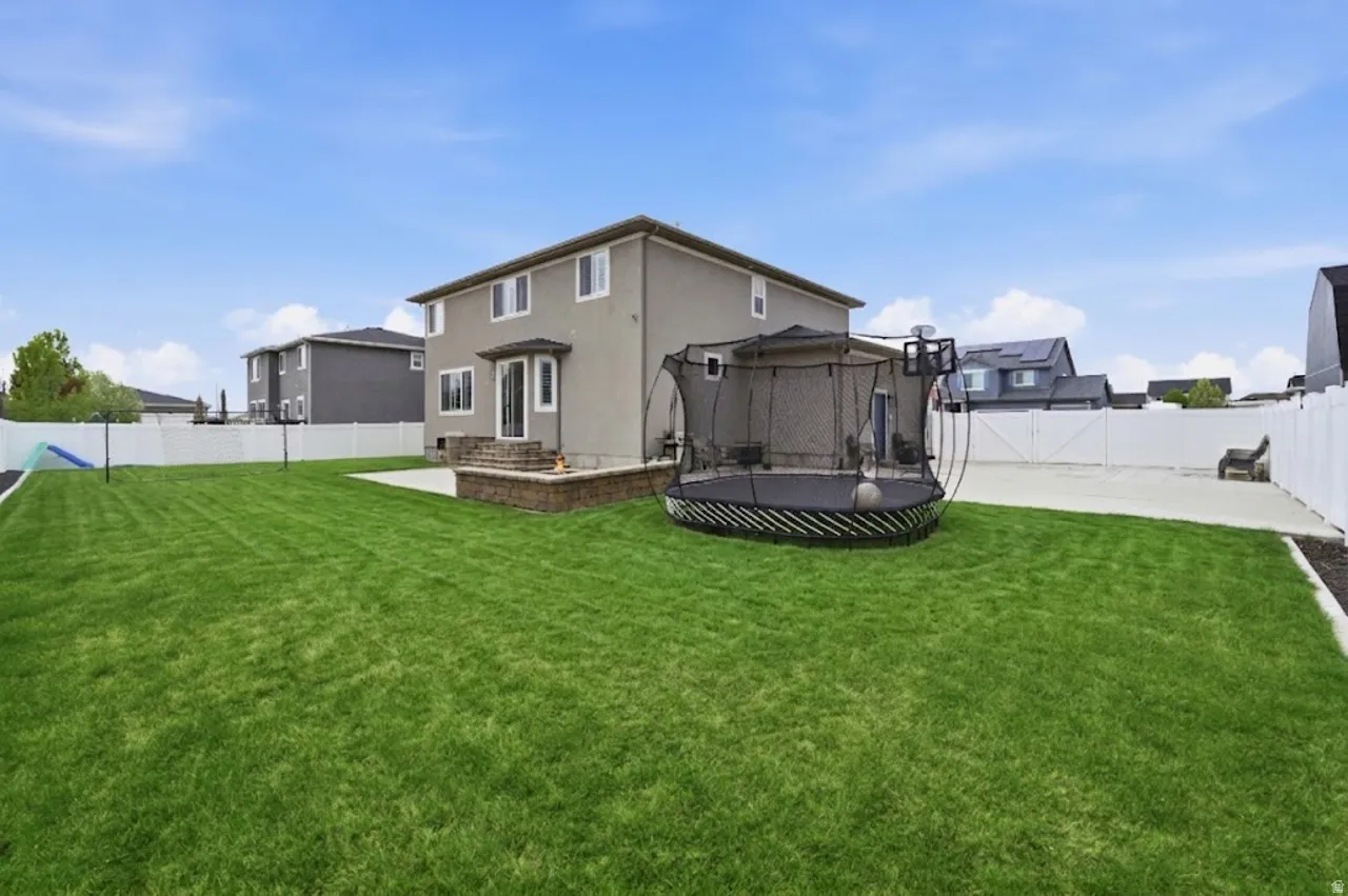 AI Enhanced Green Lawn - Back of house featuring a fenced backyard, a patio area, stucco siding, and a trampoline