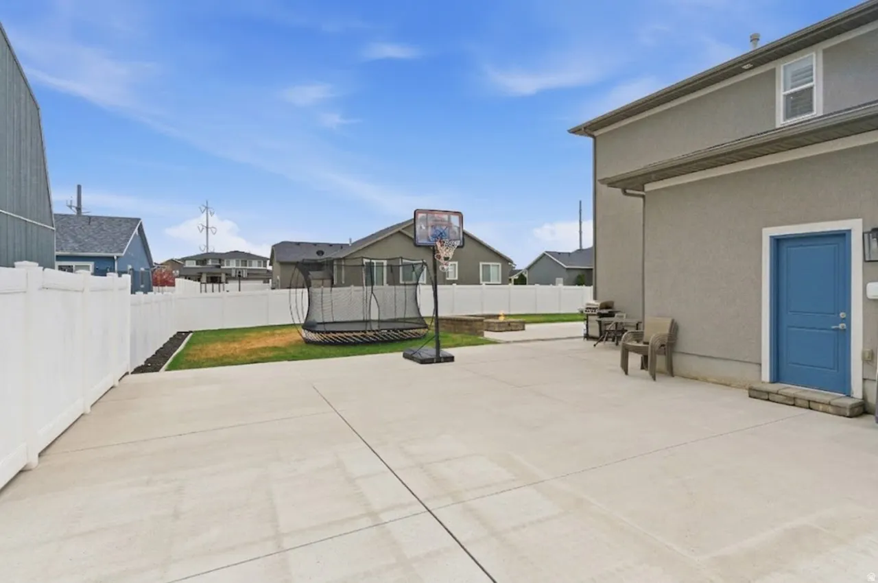 Fenced backyard with a trampoline, a patio area, a residential view, and a grill