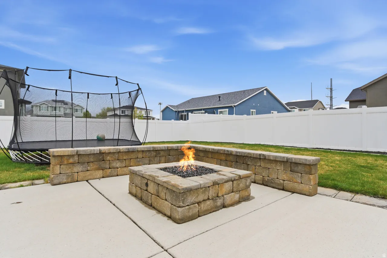 Fenced backyard featuring a trampoline, a patio, a fire pit, and a residential view