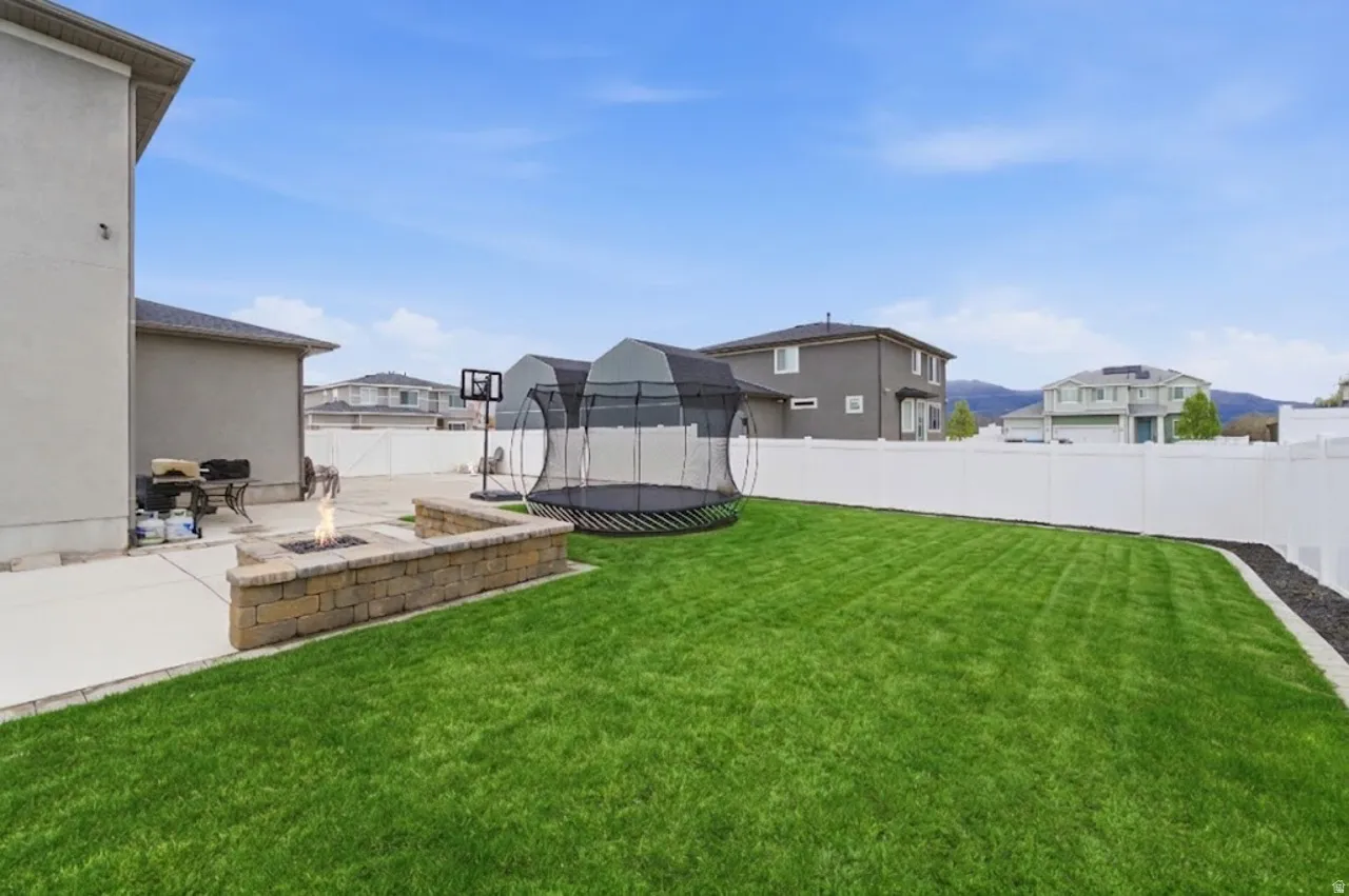 AI Enhanced Green Lawn - Fenced backyard featuring an outdoor fire pit, a patio, a residential view, and a trampoline