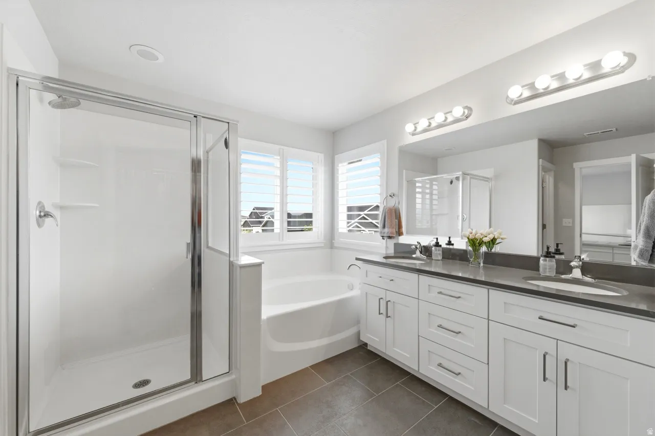Bathroom featuring a stall shower, double vanity, dark tile patterned flooring, and a bath