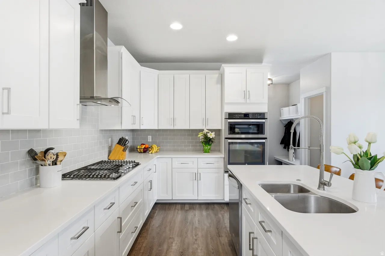 Kitchen with white cabinetry, dark wood-type flooring, stainless steel appliances, tasteful backsplash, and light stone counters
