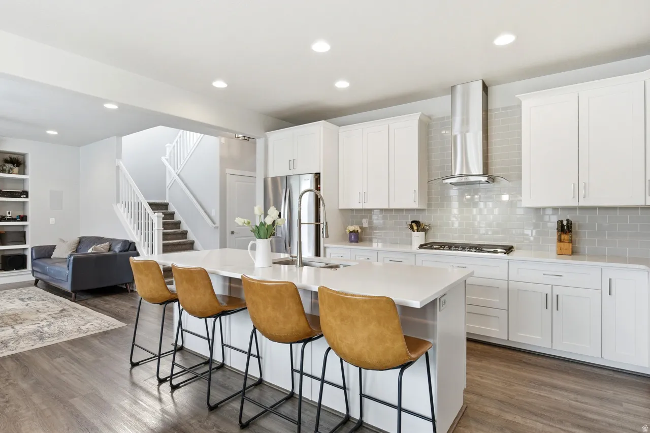 Kitchen featuring open floor plan, a kitchen bar, white cabinets, dark wood finished floors, and a kitchen island with sink