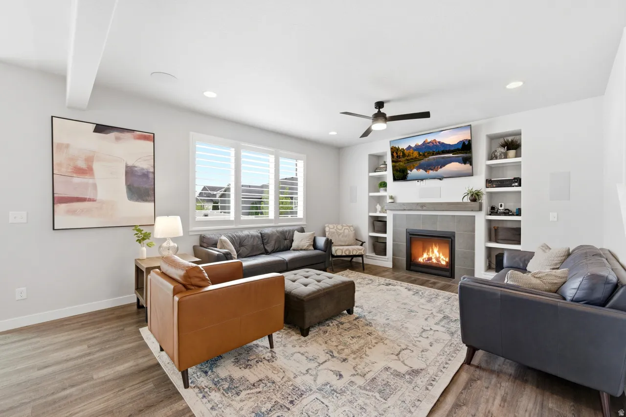 Living area with a tile fireplace, wood finished floors, a ceiling fan, recessed lighting, and built in features