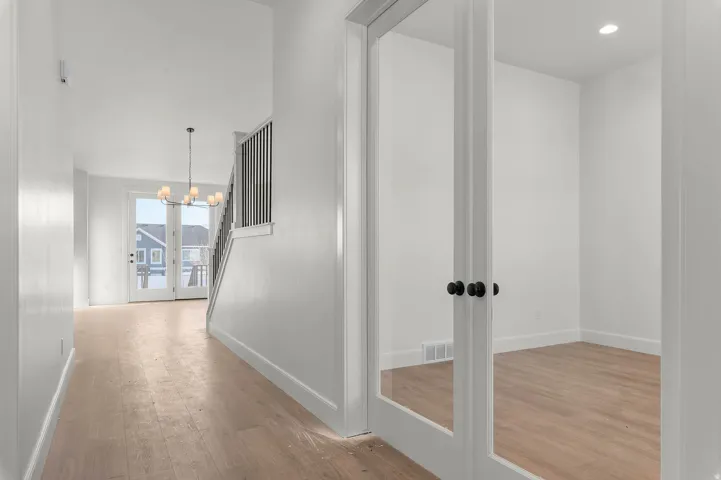 Corridor with french doors, light wood-style floors, and a chandelier