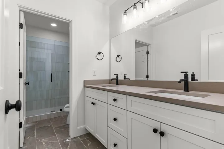 Full bathroom with double vanity, a shower stall, dark marble finish floors, and recessed lighting