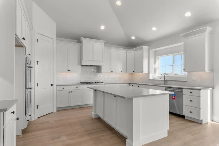 Kitchen featuring a kitchen island, white cabinetry, light wood-style floors, lofted ceiling, and stainless steel appliances