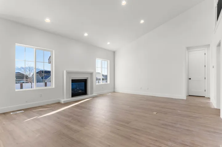 Unfurnished living room featuring recessed lighting, lofted ceiling, a glass covered fireplace, and light wood finished floors