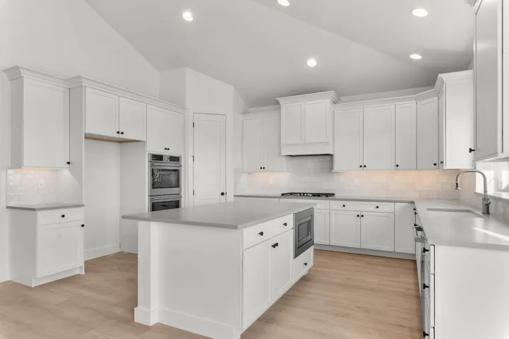 Kitchen with vaulted ceiling, light wood-style floors, a kitchen island, tasteful backsplash, and white cabinets