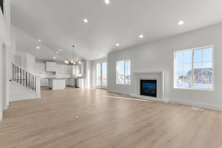 Unfurnished living room with hanging lights, light wood-type flooring, a glass covered fireplace, and vaulted ceiling
