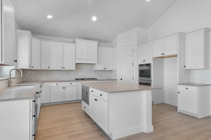 Kitchen featuring light wood-type flooring, vaulted ceiling, a center island, white cabinetry, and backsplash
