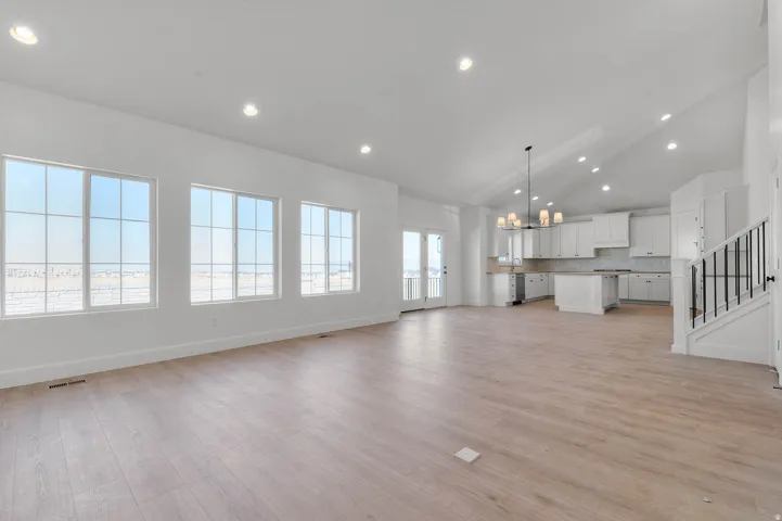 Unfurnished living room featuring suspended lighting, vaulted ceiling, and light wood finished floors
