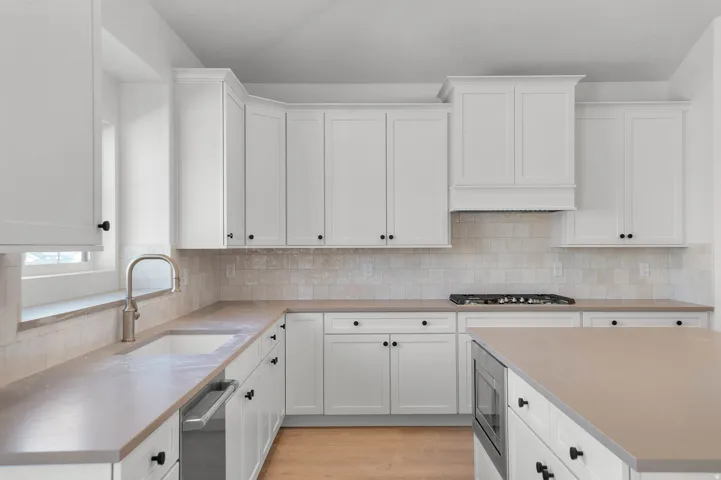 Kitchen with white cabinets, light wood-style flooring, stainless steel appliances, and tasteful backsplash
